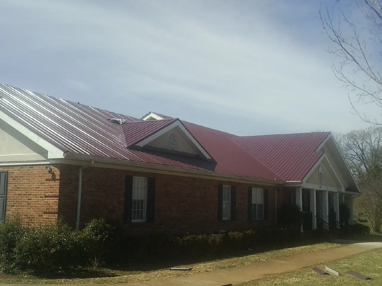 Red metal roof with gabled entries on a long brick building, from a Hail Damage Roof Repair job in Killduff