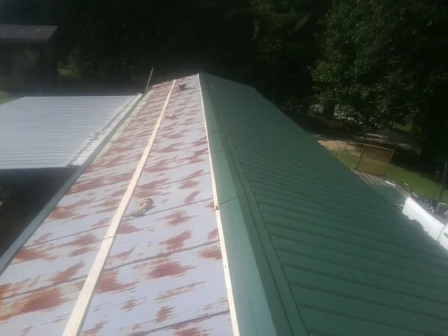 Old rusted panels beside newly installed green metal roofing — Wind Damage Roof Repair by Roofing Brothers in Killduff