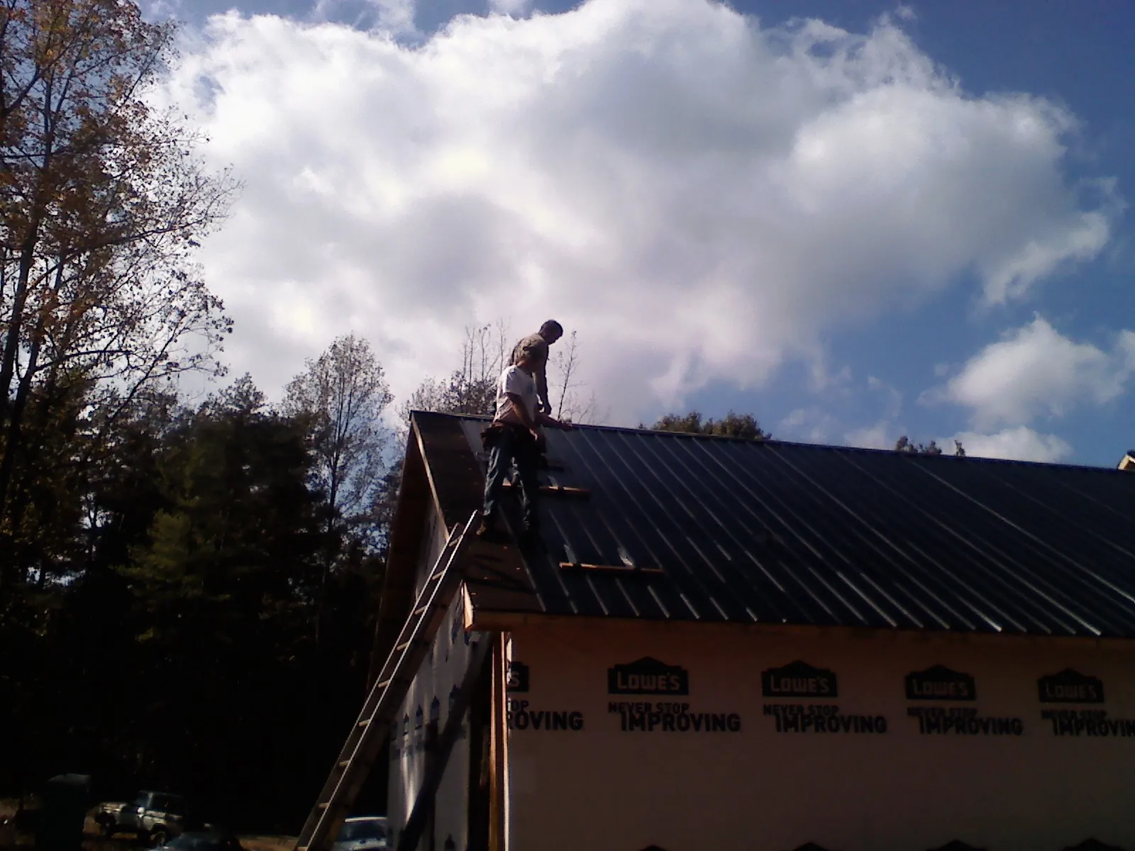 Roofer fastening dark metal panels high against a cloudy sky, from a Roof Inspection job in Killduff