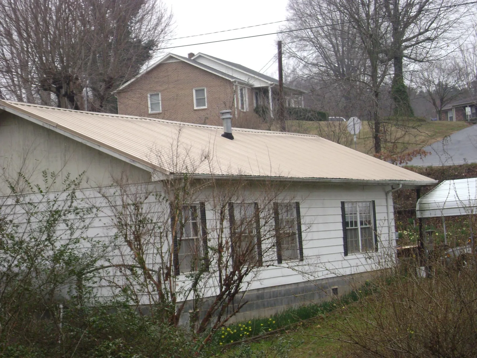 Tan metal roof on a white sided house set into a hillside — Commercial Roofing by Roofing Brothers in Killduff